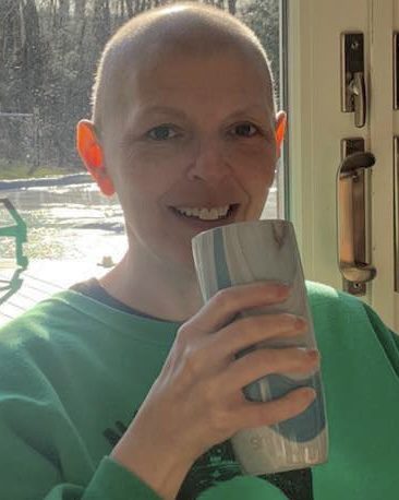 Person smiling and drinking from a cup indoors with sunlight.
