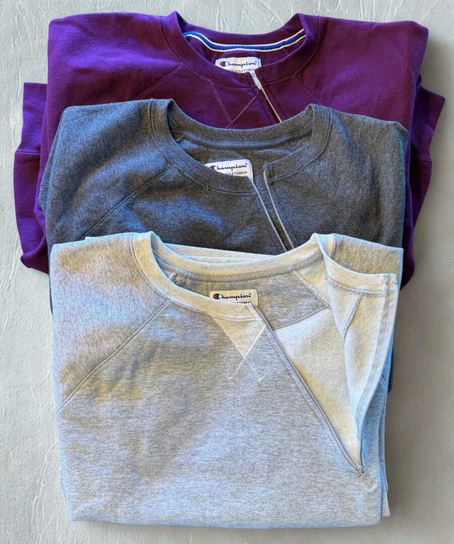 Three folded long-sleeve shirts in purple, gray, and light gray.