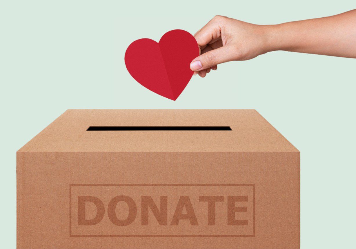 Hand placing a red heart into a donation box.
